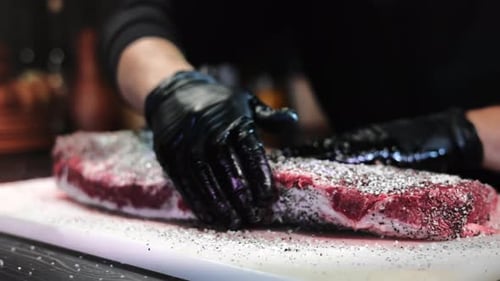 Male Chef Hands Adding Seasonings Herbs Salt Cooking Farm Meat Steak on Marble Board at Restaurant