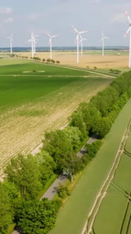 Vertical drone shot of a EV camper driving in alley in front of wind turbines