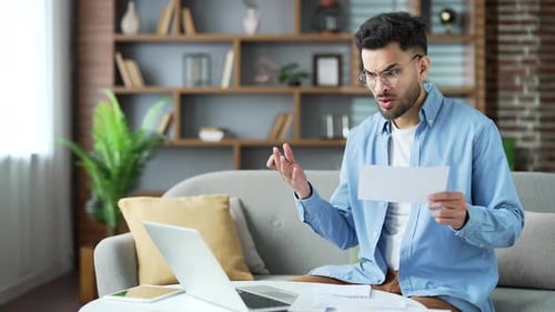 Young Adult with Laptop and Bills Looking Concerned
