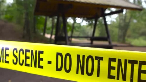 Crime scene tape pulled in front of forest trails with camping and grilling spot during cloudy day