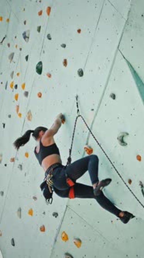 Young Woman Alpinist Practicing Climbing at Outdoor Artificial Rock Below View