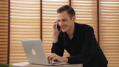 Young Adult Man Using Laptop and Talking on Phone