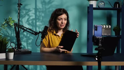 Enthusiastic Woman Presenting Tablet at Desk in Studio