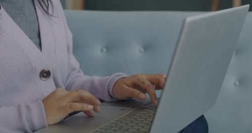 Woman Types on Laptop Indoors on Blue Couch