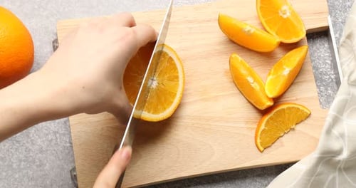 Woman cutting orange on wooden board at grey table, top view