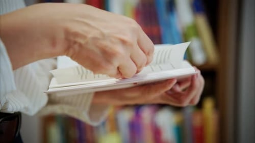 Hands Turning Pages of a Book in Library