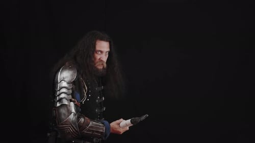 A Charismatic Man in the Armor of a Medieval Knight Hits with a Spear on a Black Background