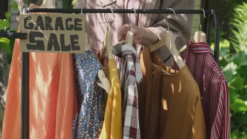 Garage Sale Person Browsing Through Clothes Hanging on Rack at Garage Sale