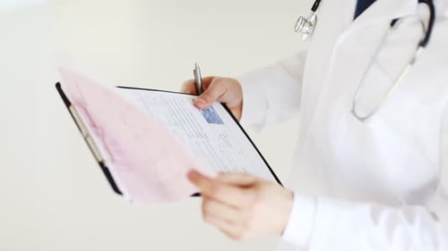 Male doctor writes prescription on clipboard in medical clinic
