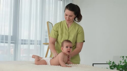 Therapist Massaging Infant on Bed in Sunny Room