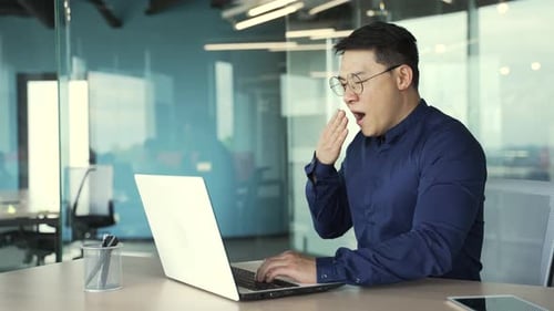 Sleepy tired businessman IT programmer with glasses having long day working on computer in the offic