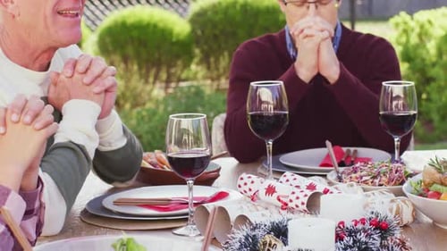 Happy caucasian family praying before dinner in garden