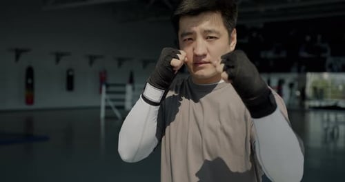 Slow Motion Portrait of Asian Man Kickboxer Standing in Gym with Wrapped Hands Up Ready for Fight