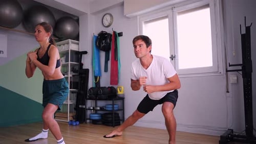Athletic man and woman performing synchronized lunge exercises together in a fitness studio, demonst