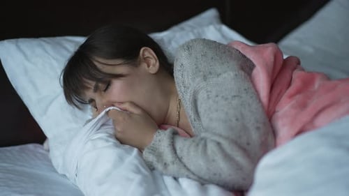 Une femme est allongée dans son lit et tousse