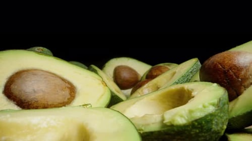 Sliced Avocado Halves with Pits are arranged on the table against a black background. Dolly slider.
