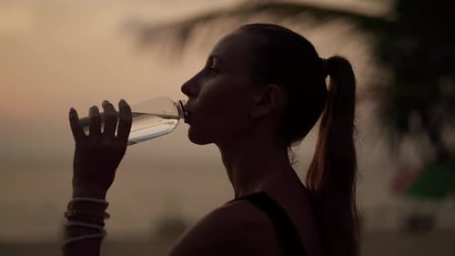Woman Drinks Water on Beach at Sunset