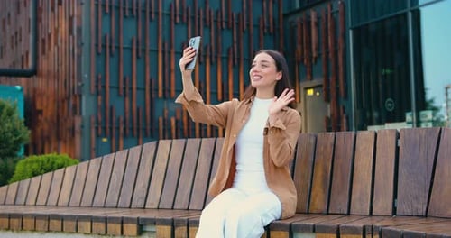 Close up of smiling Caucasian businesswoman talking on video call using phone outdoors while sitting