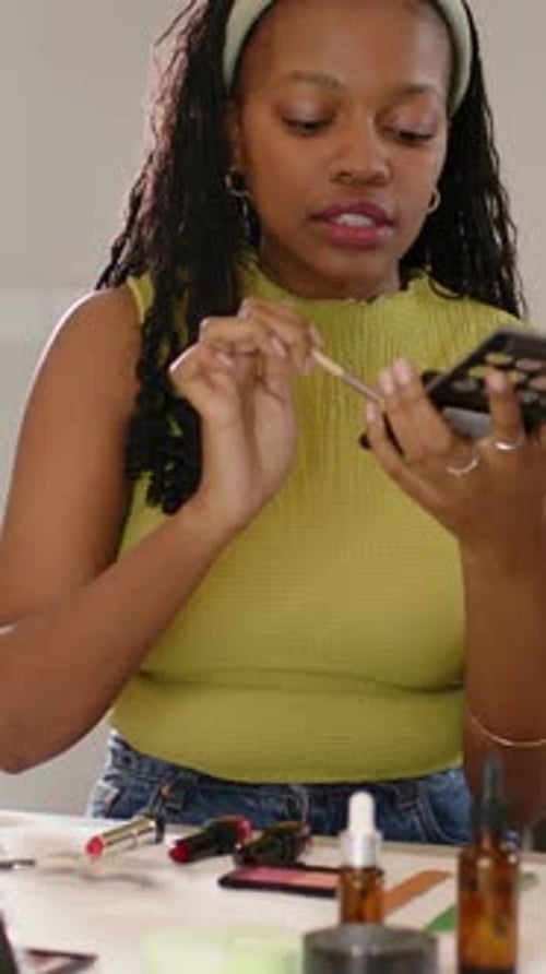 Vídeo vertical: Sosteniendo la paleta, una mujer con un top verde mostrando el maquillaje en el mostrador, brocha