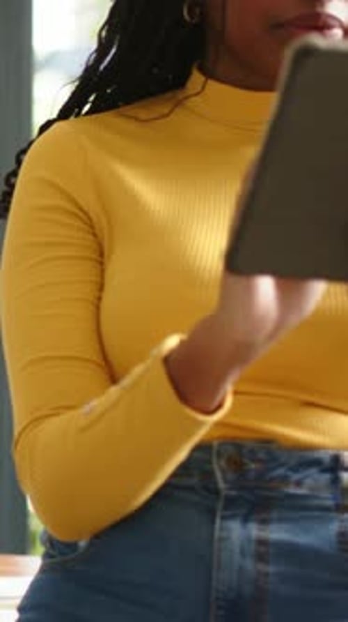 Vidéo verticale : Jetant un coup d'œil à une tablette, une femme en haut jaune tapant en haut à la maison, des documents, un espace de copie