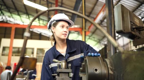 Eine Fabrikarbeiterin richtet in der Werkstatt eine CNC-Drehmaschine ein.