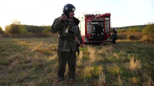 Professional Fireman in Full Equipment Talking on Walkietalkie on Place at Fire Near a Big Red Truck