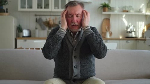Man Massaging Temples, Seeking Headache Relief at Home