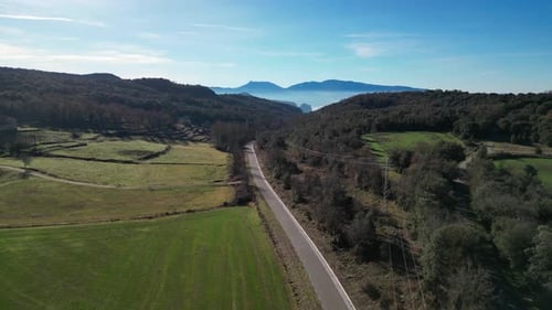 Carretera panorámica que serpentea a través de exuberantes campos verdes y colinas boscosas bajo un cielo azul claro
