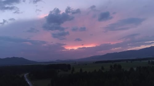 Aerial Over the Forest and Road in the Valley Between Mountains at Beautiful Pink Sunset