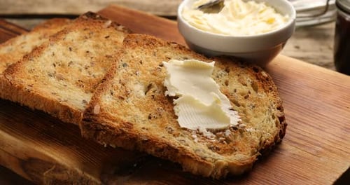 Butter Being Spread on Grain Toast on Board