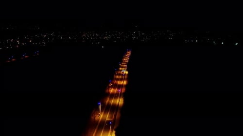 Aerial night view of a lit highway stretching into city lights, cars in motion, urban vibe