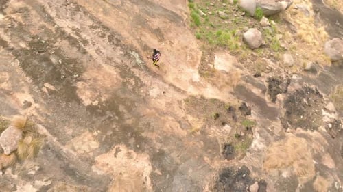 A birds eye view shot of an African man rock climbing up a granite rock in Africa.