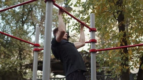 Sportsman Doing Exercises on a Pullup Bar in the Summer on a City Sport Ground Young Caucasian