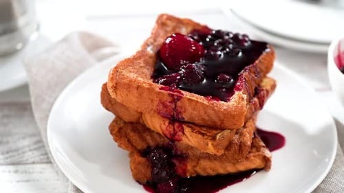 Garnishing Stack of Freshly Made French Toast Garnished with Mix Berry Compote and Powder Sugar