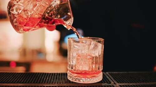 A close up shot of a freshly mixed cocktail flowing from a crystal mixing glass into a tumbler fille