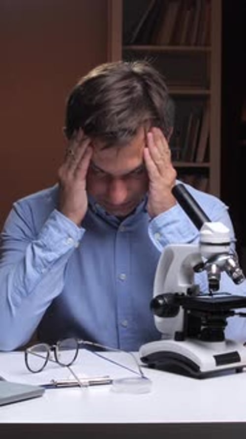 Stressed Man at Desk with Microscope