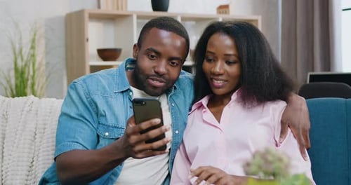 Smiling Couple Using Smartphones on Sofa at Home