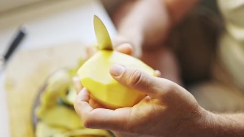 Chef Peeling Potato with Knife on Cutting Board