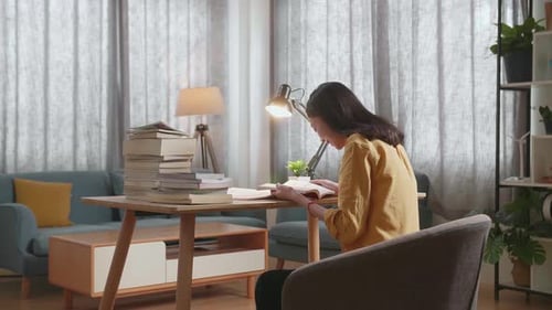 Side View Of Young Asian Female Reading Books While Studying At Home