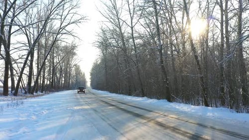 Une voiture noire roule rapidement sur une route glacée recouverte de neige. Un VUS emprunte une route de campagne déserte en hiver