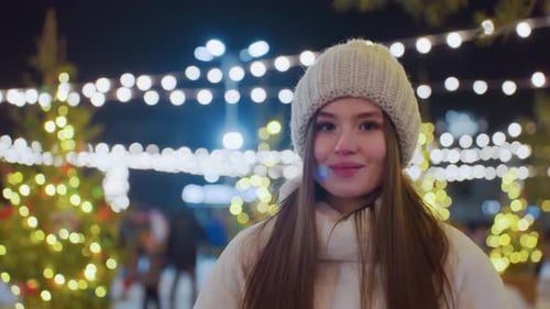 Smiling Woman in White Beanie and Fluffy Jacket Under Festive Lights