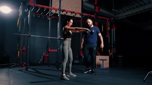beautiful young fitness woman doing exercises with dumbbells in hands with trainer in gym