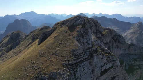 Die Drohne fliegt auf den Gipfel eines Berges, der von der Sonne beleuchtet und von Bergketten umgeben ist