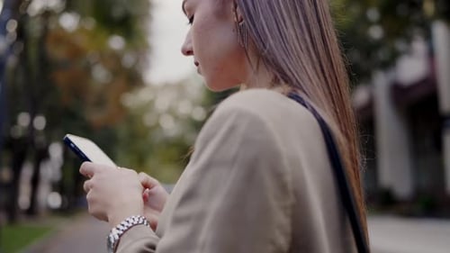 Young Woman Texting on Her Phone While Walking in the City