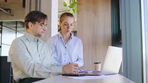 Two Business Professionals Have a Productive Discussion Over a Laptop in a Modern Office Sharing