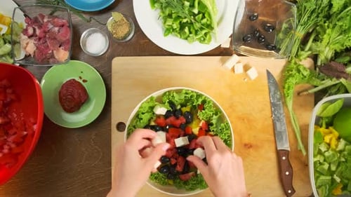 Hands woman chef make fresh vegetable salad, sprinkling the plate with chopped feta cheese, close-up