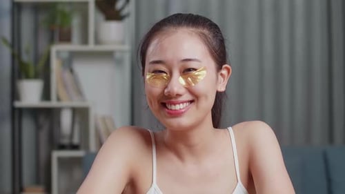 Close Up Of Asian Woman Applying Under Eye Patches And Smiling To Camera While Taking Care Skin