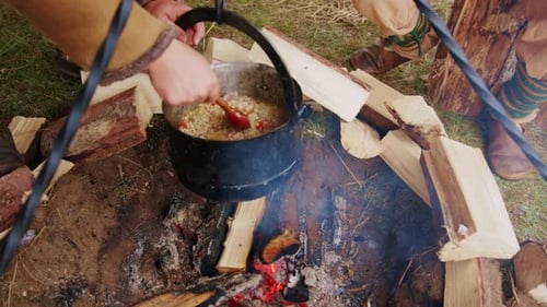 People wearing medieval costumes preparing a delicious dish on campfire