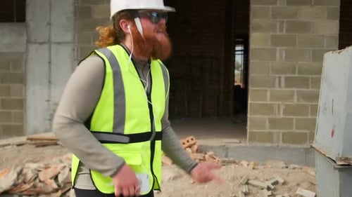 Engenheiro dançarino com barba ruiva no canteiro de obras no final do dia tocando guitarra aérea,