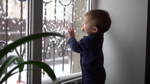 A Oneyearold Boy Stands at the Window of the House